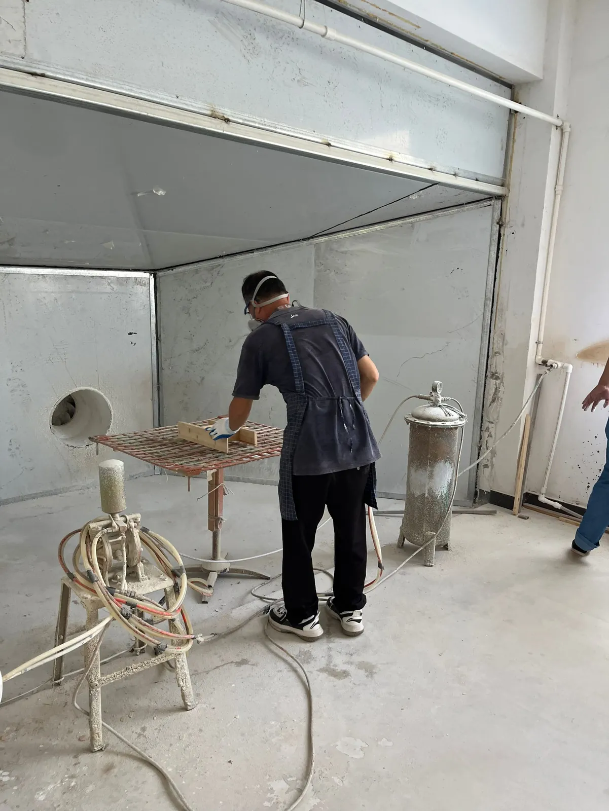 Worker in protective mask spraying wooden parts in a spray booth