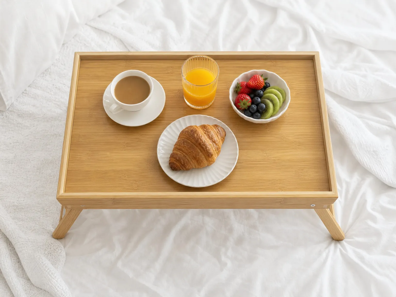 Overhead view of a bamboo bed tray with coffee, juice, croissant and fruit bowl