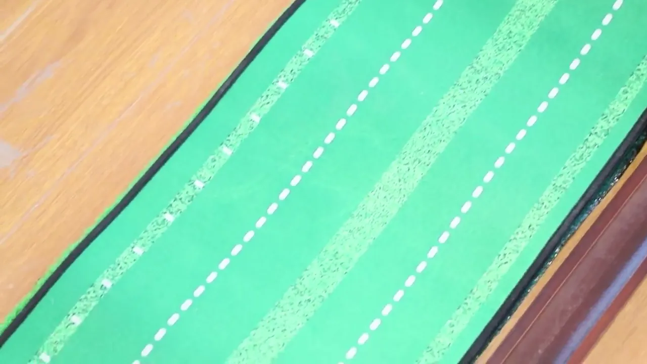 Close-up of the green felt playing surface of a putting mat with white guide lines
