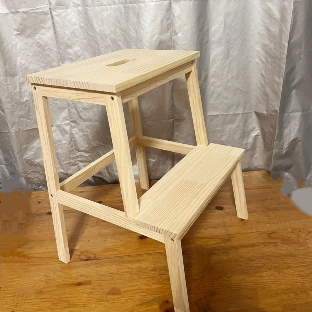 Two-step pine step stool photographed on a wooden floor against a grey backdrop